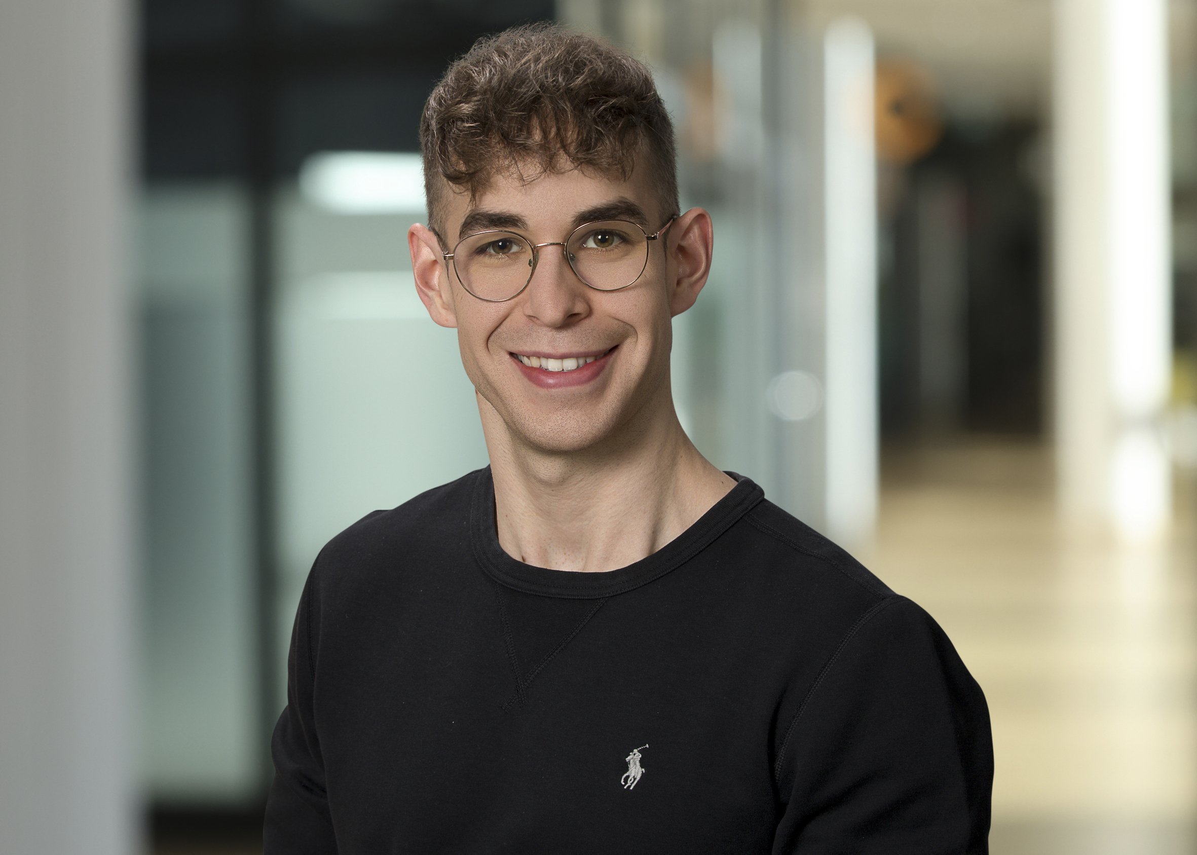 Portrait junger Mann mit kurzen welligen Haar und Brille im schwarzem Rundhals Pullover