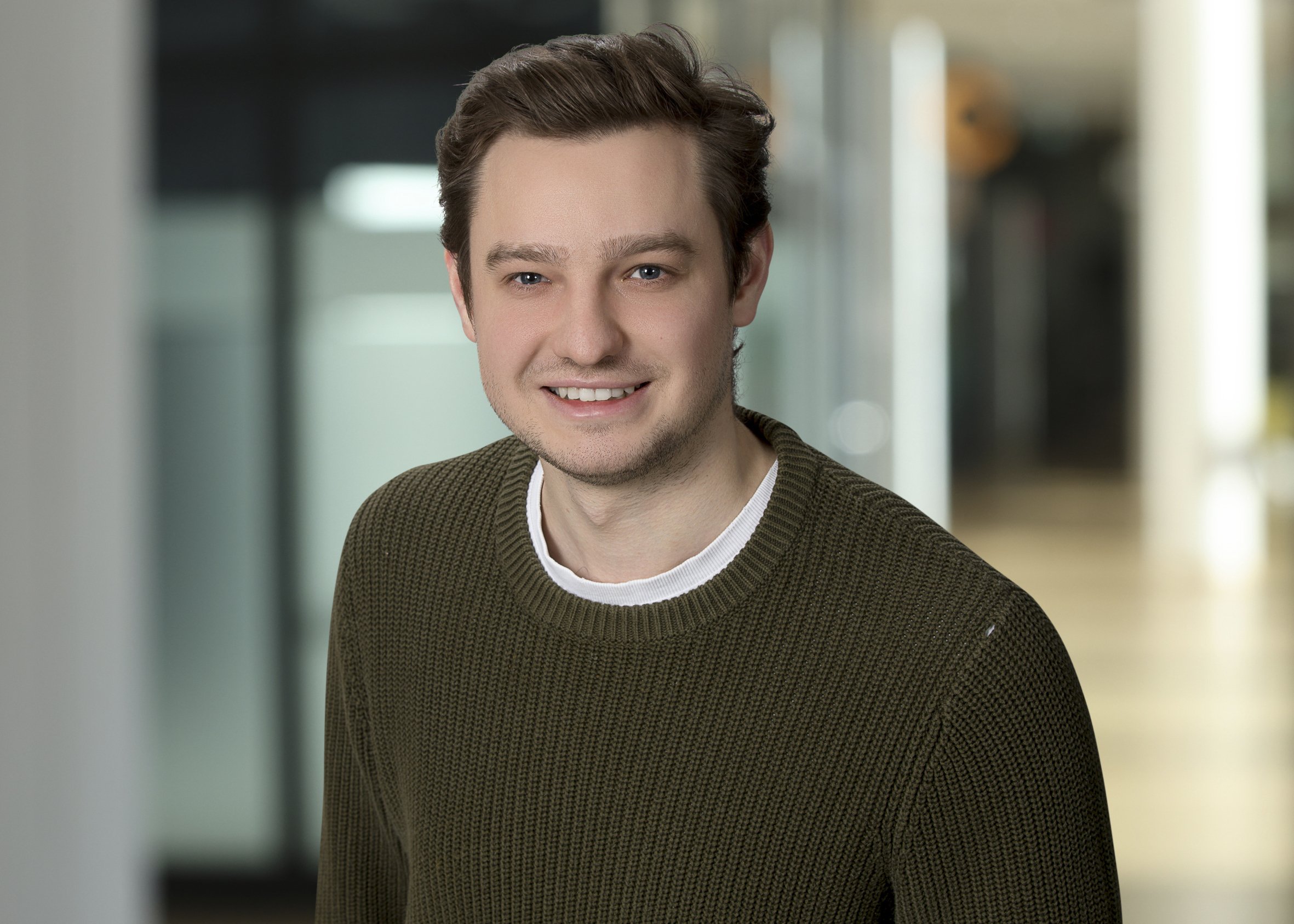 Portrait junger Mann mit kurzen dunklen Haaren und olivegrünen Strickpullover