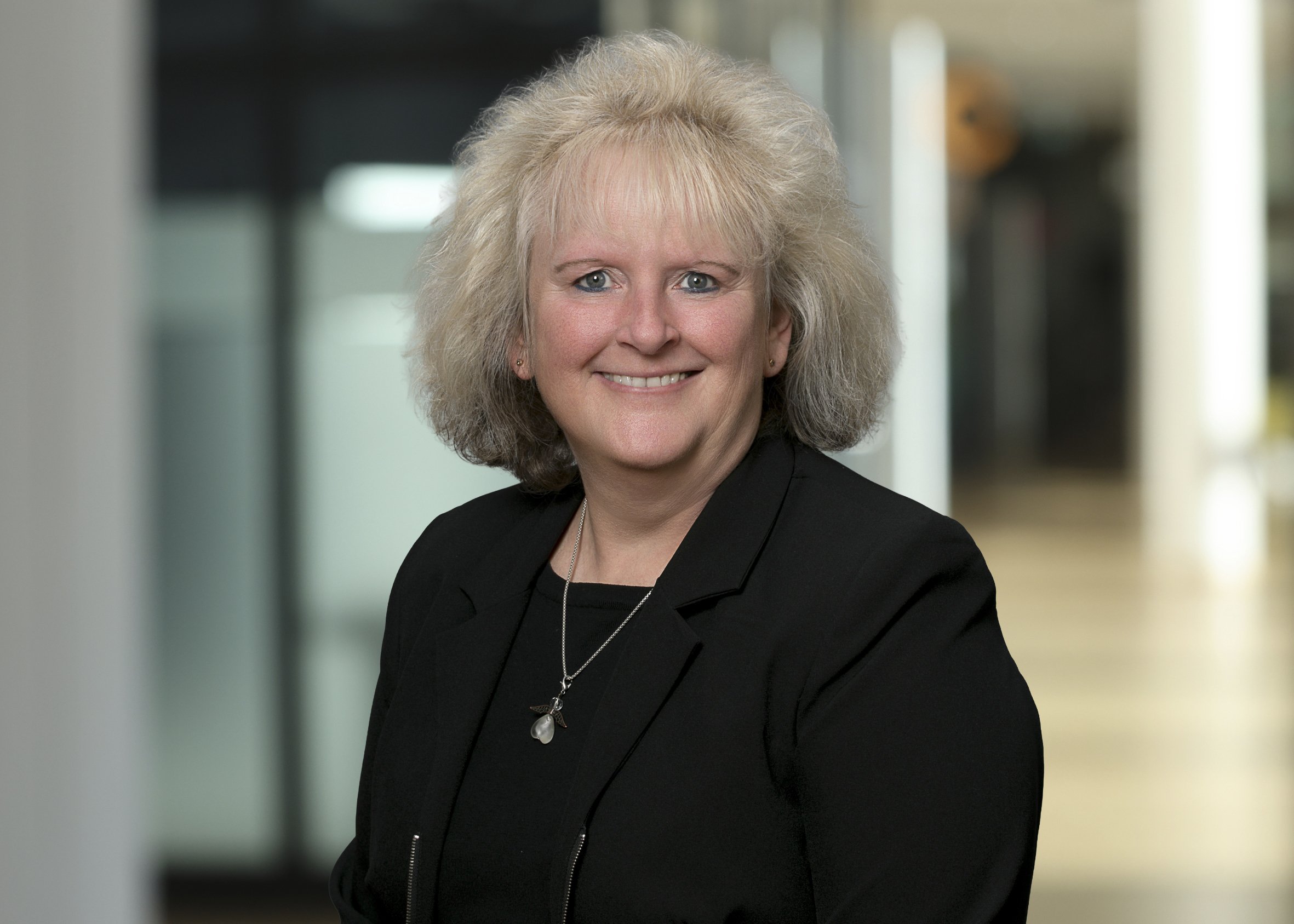 Portrait Frau mittleren Alters mit blonden schulterlagen Haaren im schwarzen Blazer mit schwarzem Shirt